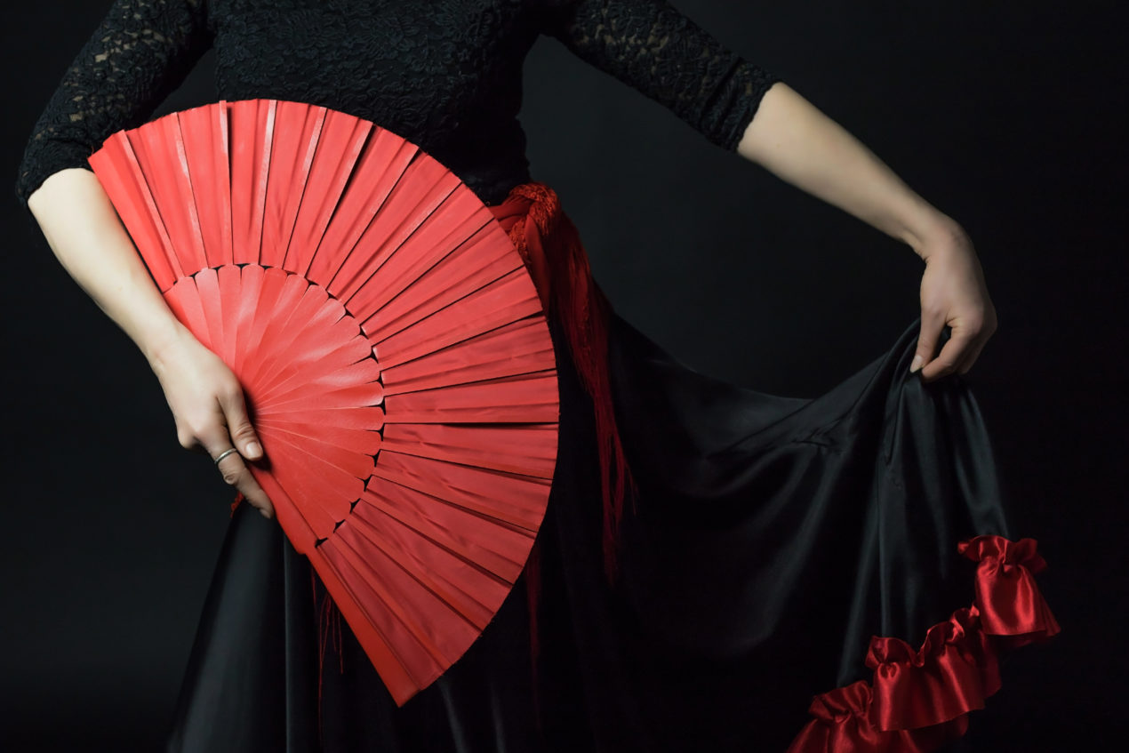 Low Key photo of Flamenco Dancer middle age woman holding red fan and her skirt.