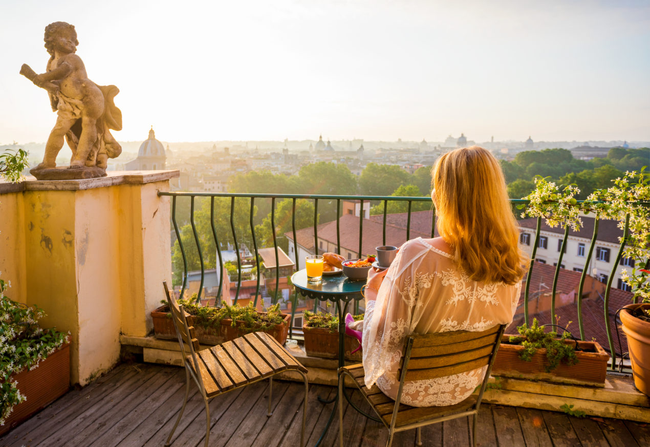 Woman sitting on a balcony overlooking an Italian city - example of hotel accommodations in Italy