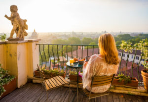 Woman sitting on a balcony overlooking an Italian city - example of hotel accommodations in Italy