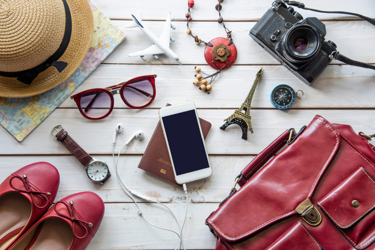 selection of travel accessories including iphone, shoes, glasses, hat, camera, purse