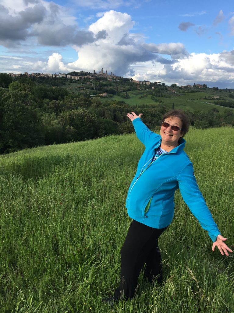 Author Carol Cram in the Tuscan countryside with the town of San Gimignano in the background