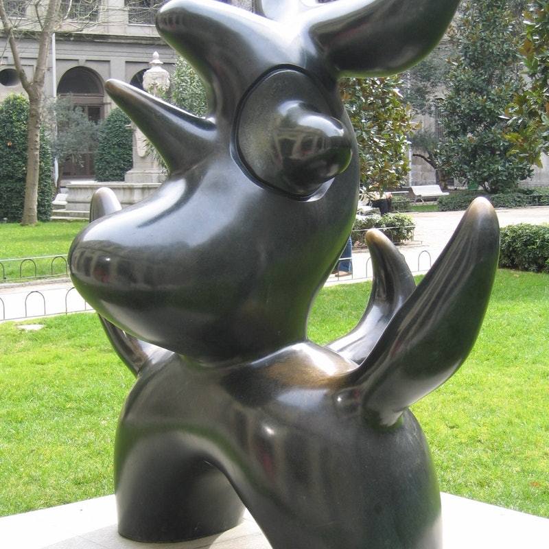 A black, abstract sculpture by Joan Miró, featuring curved shapes and smooth surfaces, sits on green grass at the Reina Sofia Museum in Madrid.