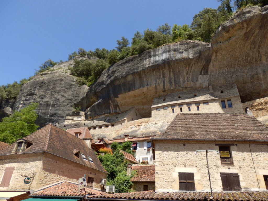 Houses in the town of Les Eyzies, Dordogne, France under the shadow of overhanging limestone cliffs. It's one of my recommended places to visit in France.