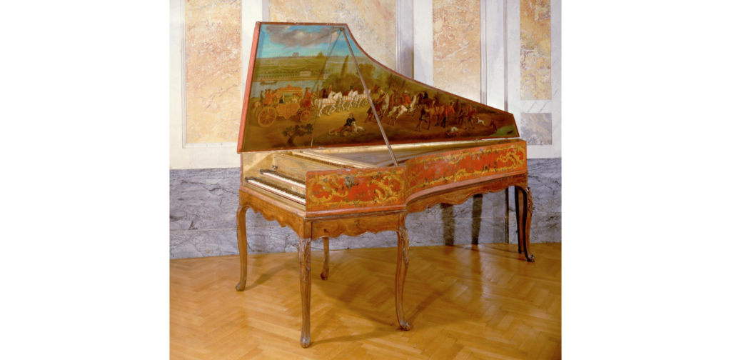 A vintage harpsichord with ornate red and gold detailing, standing in a room with marble walls and wooden floors. The harpsichord’s lid features a painting of a pastoral scene with horses and figures.