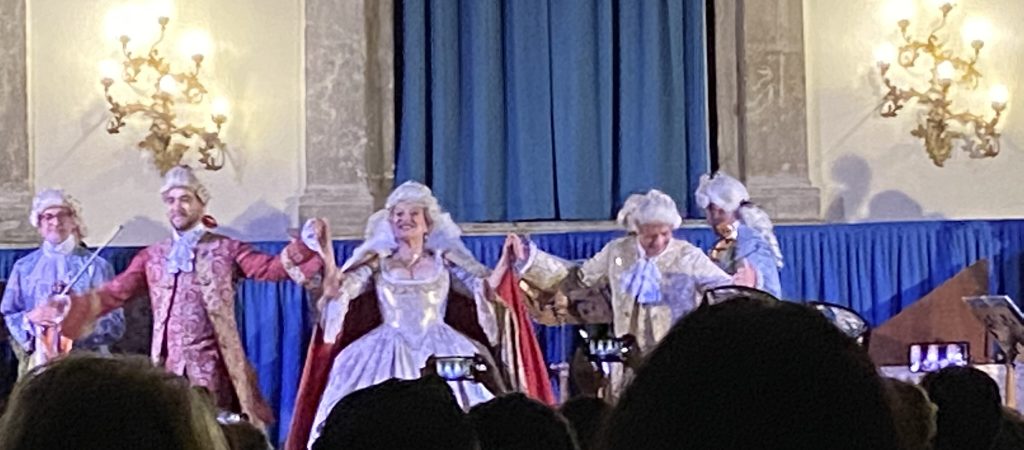 Performers wearing eighteenth century costumes and wigs taking a bow after a concert performance in Venice.