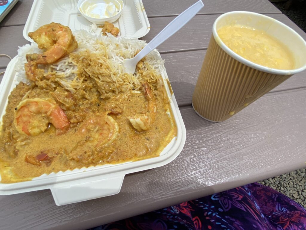 Take-out container filled with creamy coconut curry next to a cup of mango lassi