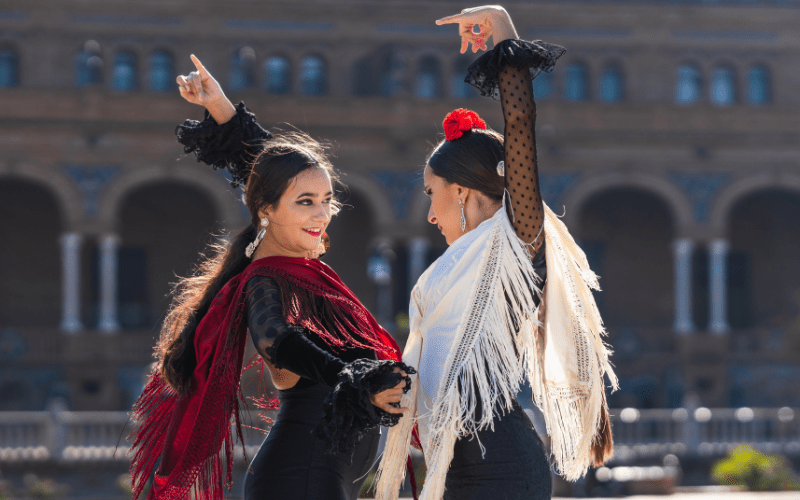 Two female flamenco dances dancing outside against a backdrop of rounded columns in Seville.