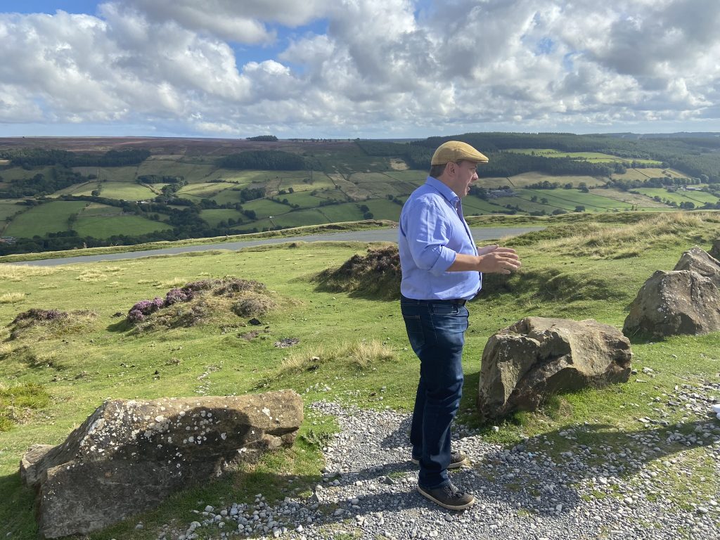 A man talking about moorland on a hill overlooking a spectacular view of moors in Yorkshire