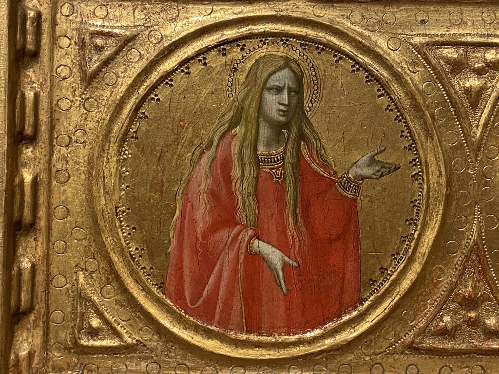 Medieval gold panel that includes a portrait of a female saint dressed in a red robe and with long hair, and created by Fra Angelico included in the Medieval collection at the Courtauld Gallery in London.
