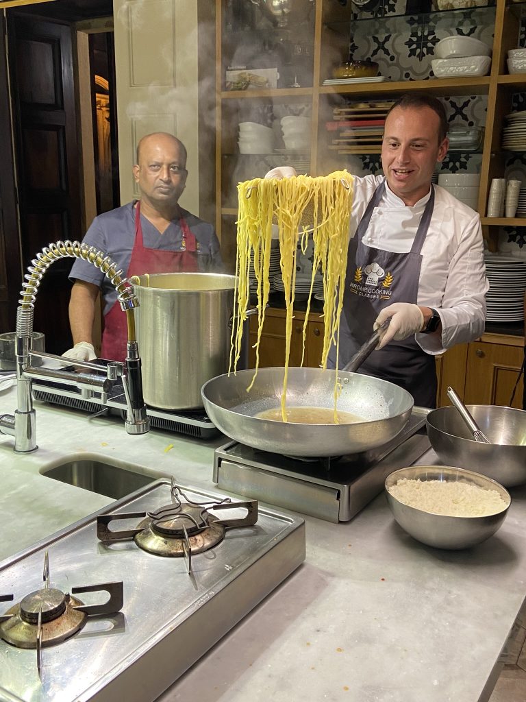 Chef Marco at InRome Cooking school adding spaghetti to a sauce.
