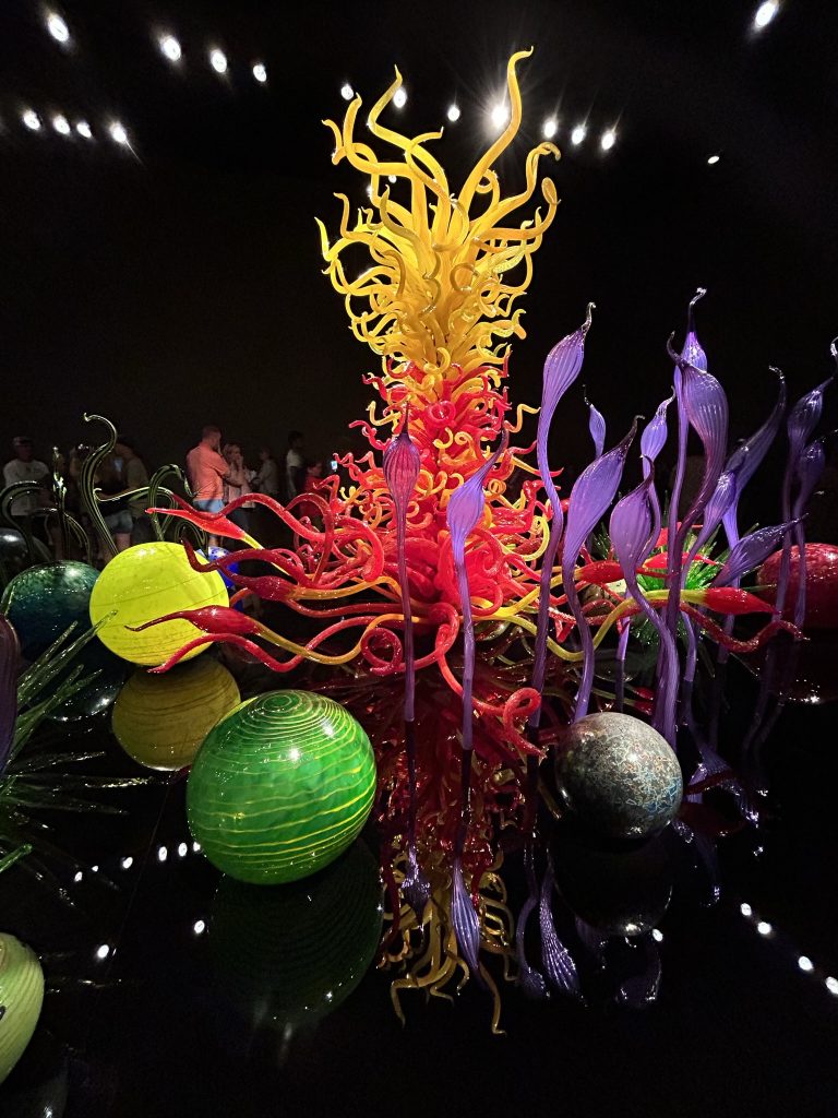 Chihuly bright and colorful red and yellow glass sculpture with tall purple fronds and large orbs