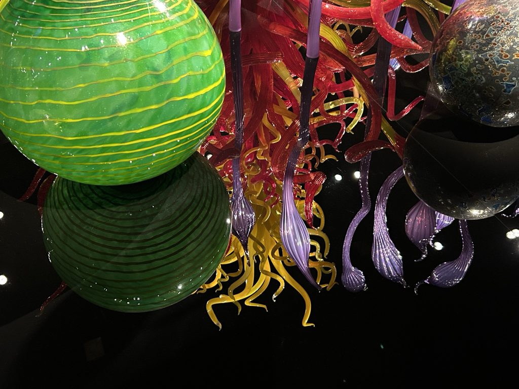 Chihuly bright and colorful sculptures with green orb and a reflection of a large twisted red and yellow glass sculpture