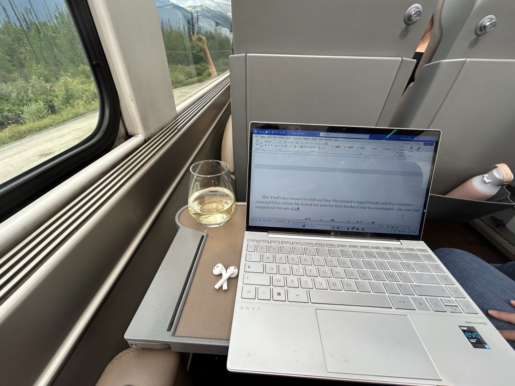 A laptop and a glass of wine on a tray table on the Rocky Mountaineer