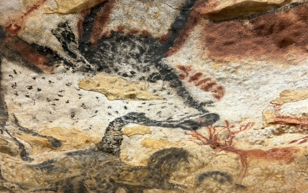 A detailed view of a prehistoric painting in Lascaux IV in the Dordogne. The painting depicts a spotted bull with black and red details, surrounded by abstract shapes and natural rock textures. The artwork demonstrates the expressive techniques used in ancient cave art.
