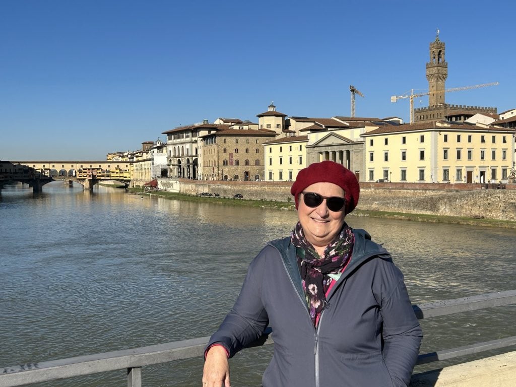 Carol Cram standing by a bridge over the Arno in Florence. It's November and she's wearing a tam and coat.