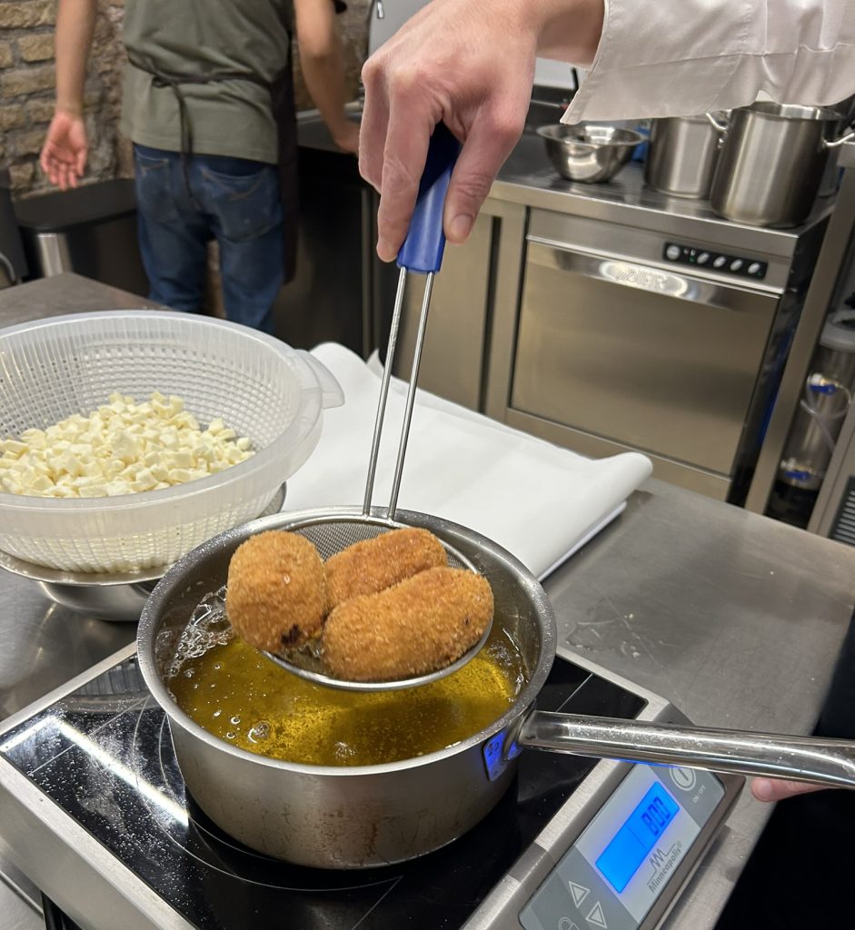 Hands shaping rice mixed with tomatoes around fresh mozzarella cubes, crafting traditional Roman suppli in a cooking class.