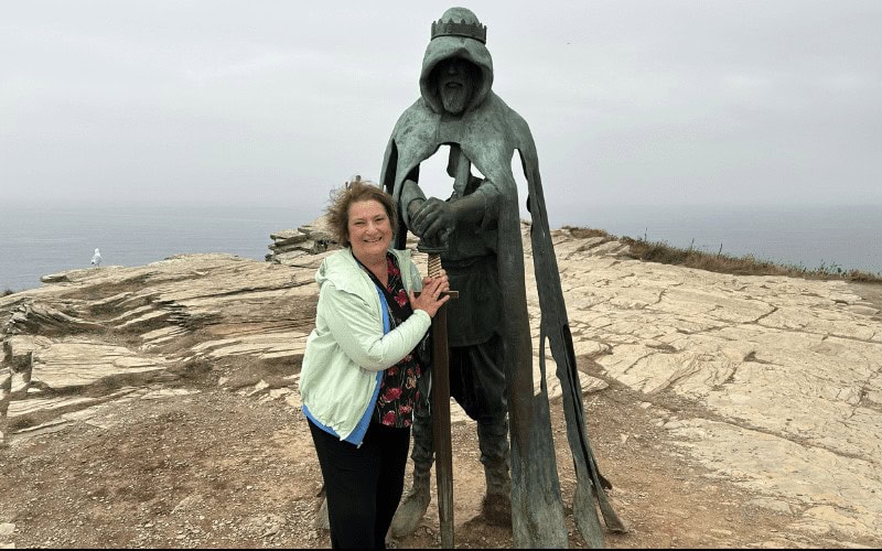 Carol Cram in front of a statue of King Arthur at Tintagel in Cornwall, England.