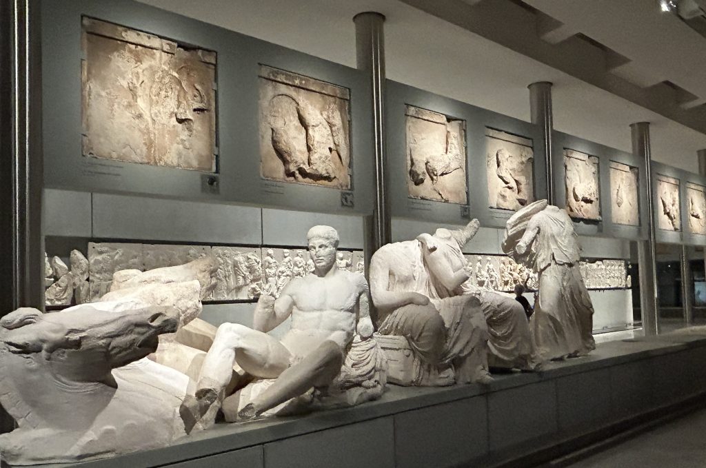 Portion of the frieze that once adorned the Parthenon at the Acropolis exhibited in the Acropolis Museum in Athens. This portion shows a marble statue of a man reclining next to another seated man without a head.