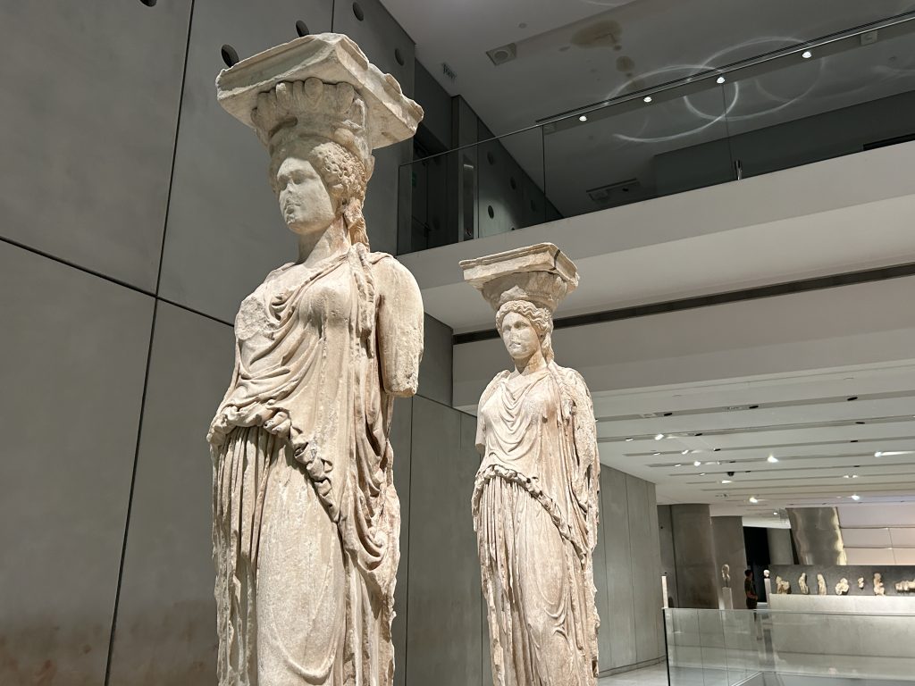 Close up view of two of the female statues wearing Greek robes with pediments on top of their heads. These are two of the original columns used to hold up the Erechtheion Temple on the Acropolis, and are very classically Greek and beautiful.