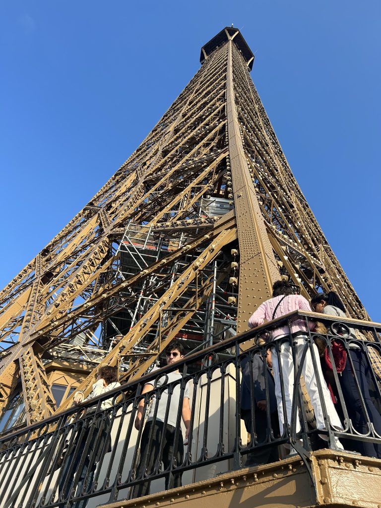 A dramatic upward perspective of the Eiffel Tower from the second level, showcasing its intricate ironwork against a clear blue sky.