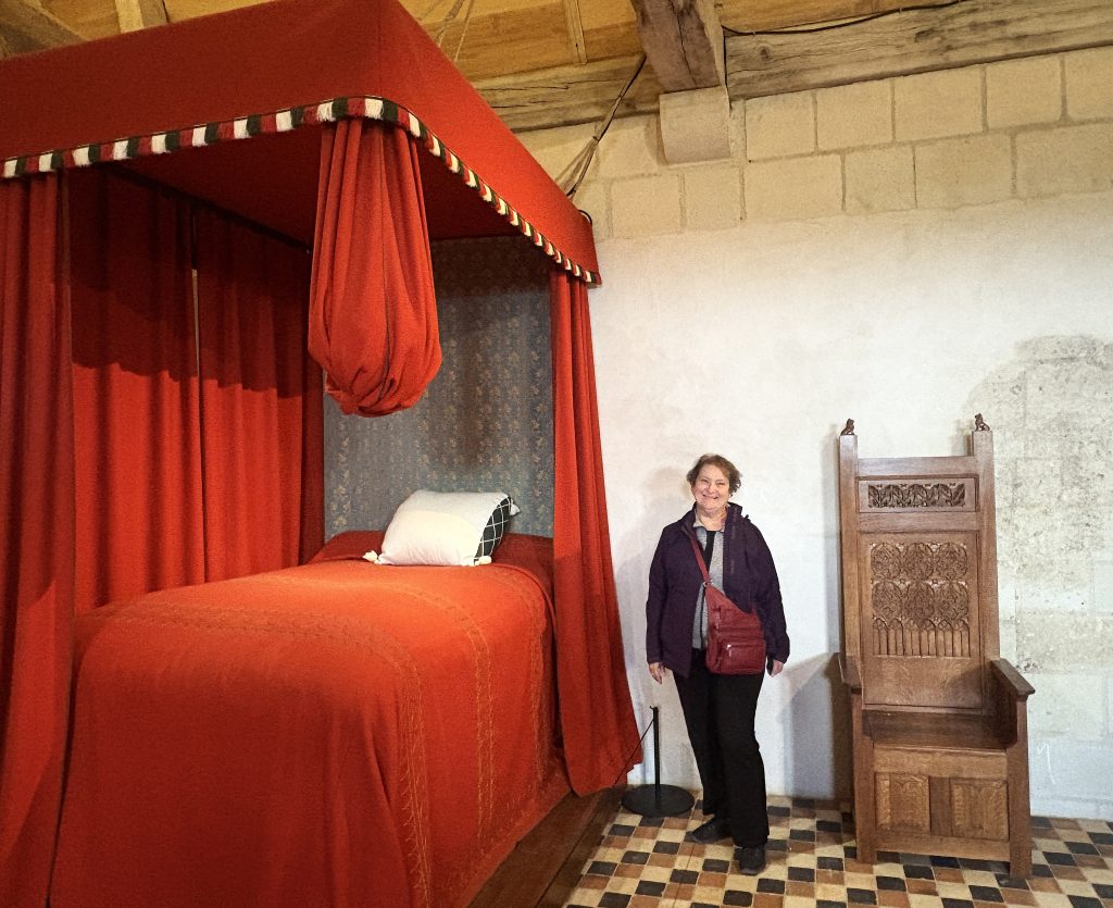 A visitor stands beside a four-poster canopy bed draped in red fabric at Château de Chinon, a Loire Valley château steeped in royal history and medieval charm.

