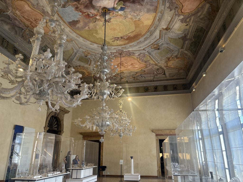 glass chandelier hanging from elaborately painting ceiling in a palazzo housing the glass Museum on Murano