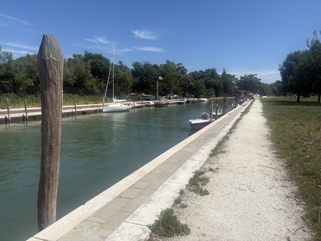 Tranquil sidew canal in Murano with just a few boats and no people and plenty of trees