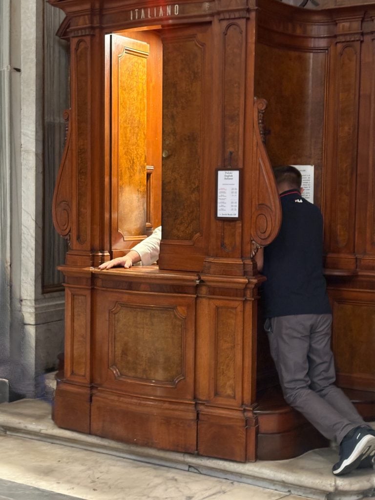 View of a confessional with a person confessing and the hand of the priest appearing at the window taken  on a Photography Tour in Rome with Rome Photo Fun Tours.