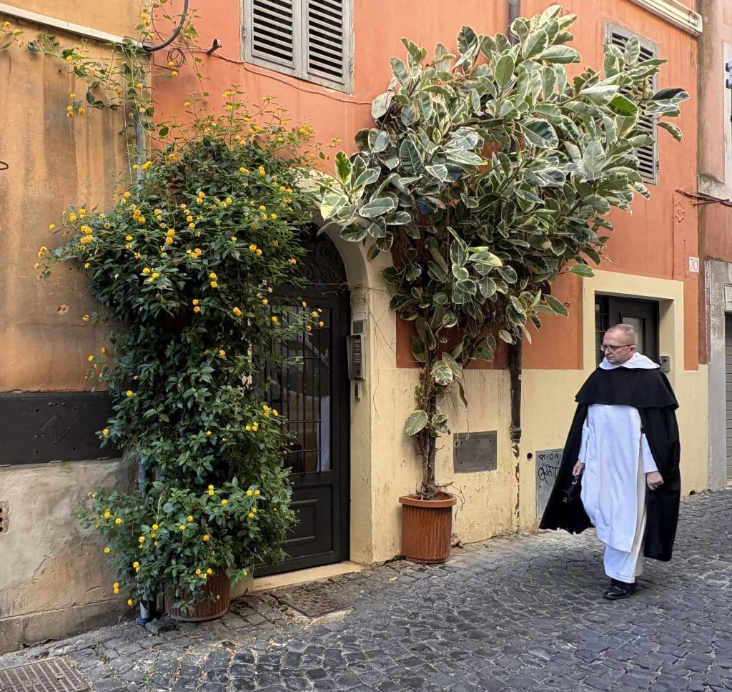 A priest walking along a quaint cobbled street past a house with vegetation growing up it  taken  on a Rome Photography Tour with Rome Photo Fun Tours.
