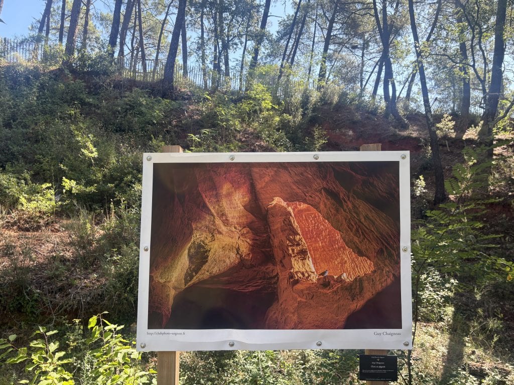 Photograph of ochre cliffs mounted on an easel and displayed against a backdrop of trees in the luberon area of france  