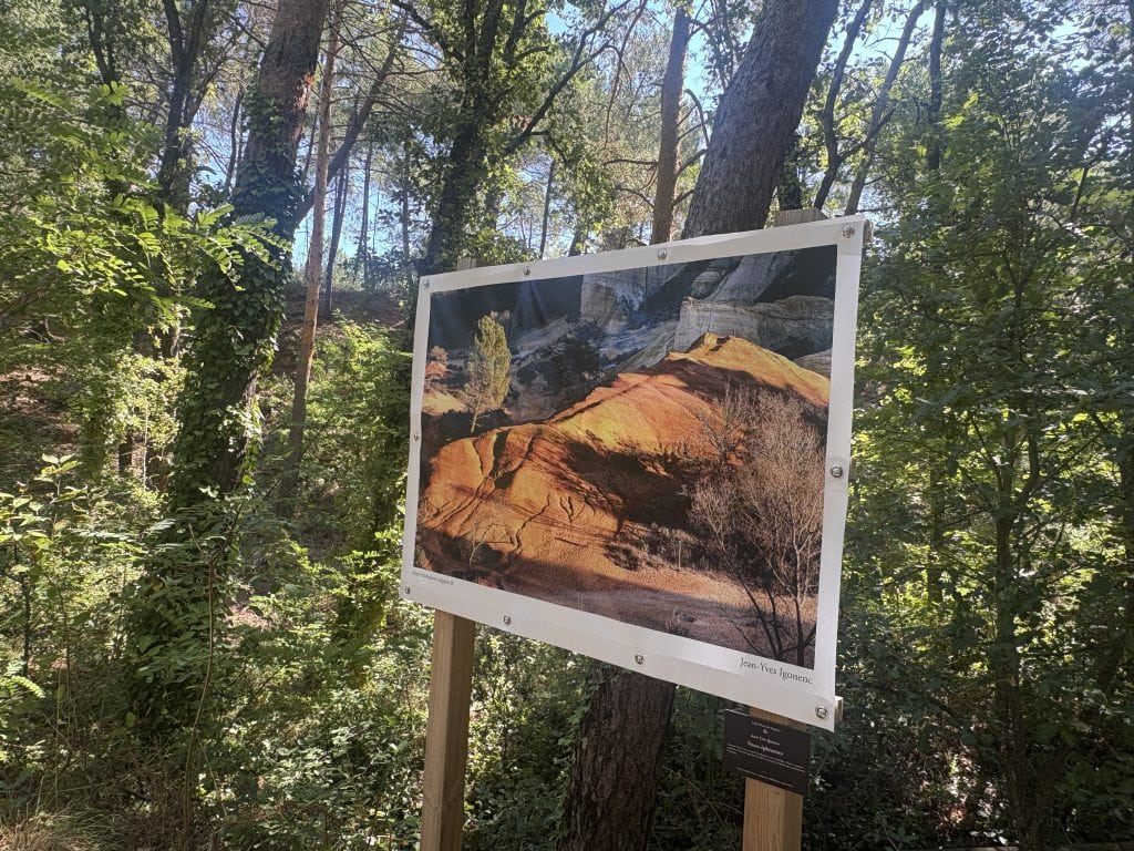 Photograph of ochre cliffs mounted on an easel and displayed against a backdrop of trees in the luberon area of france  
