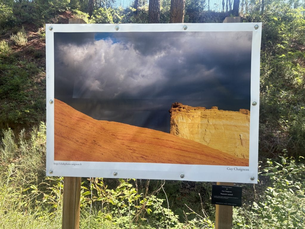 Photograph of ochre cliffs mounted on an easel and displayed against a backdrop of trees in the luberon area of france  