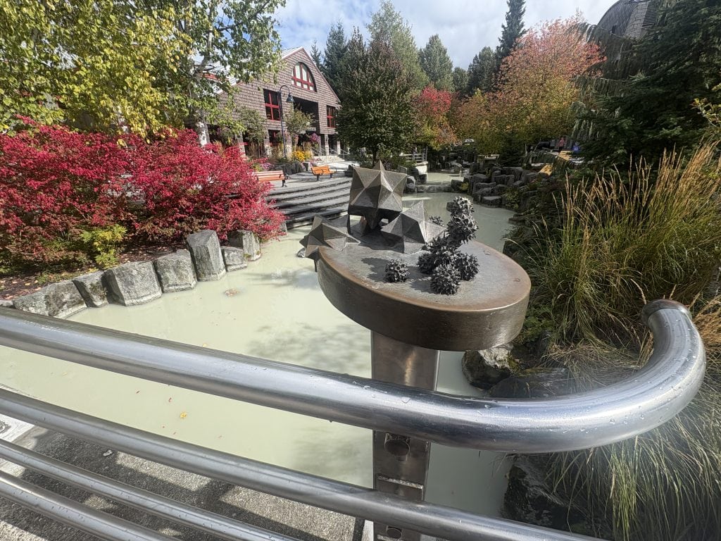 View of Whistler creek with autumn colors and a metal sculpture in the foreground