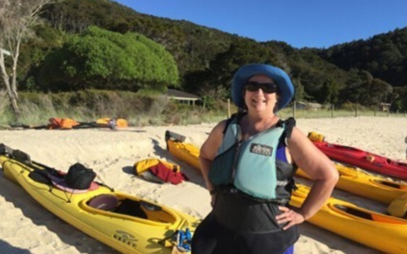 Carol Cram in front of a kayak on the beach in Abel Tasman National Park in New Zealand