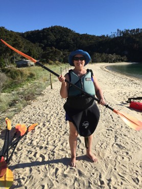 Carol Cram wearing a kayak skirt and holding a paddle on the beach at Abel Tasman National Park in New Zealand