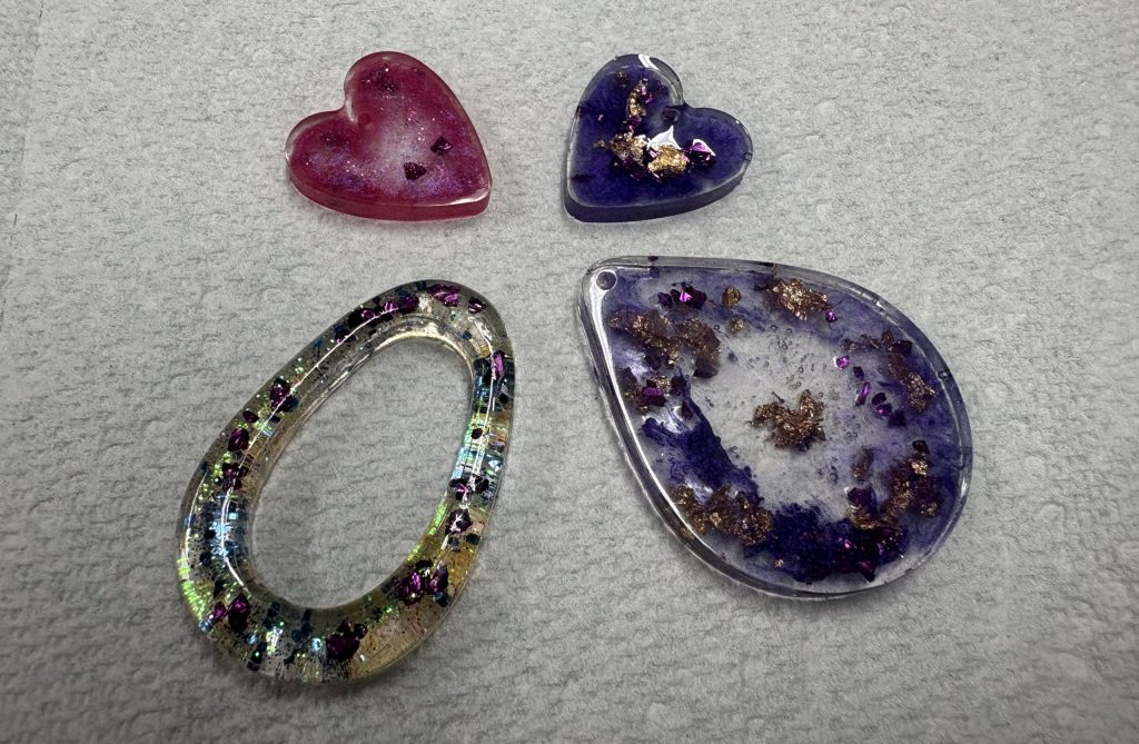 Four piecxes of resin art jewelry - two small hearts - one is pink and one is purple and two larger pendants