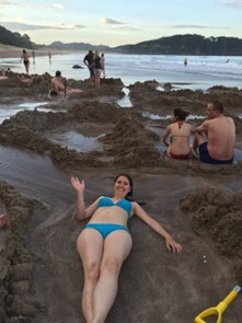 Julia Simpson lying in sand on hot water beach on the Coromandel Peninsula, one of the wonderful sites to discover on New Zealand's North Island