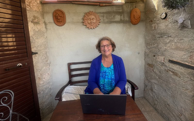 Carol Cram sitting in front of a computer in a Tuscan home while on a writing retreat in Tuscany