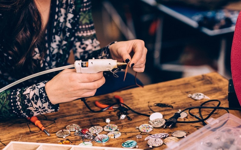 Two hands holding a jewelry drill and making jewelry to represent crafts