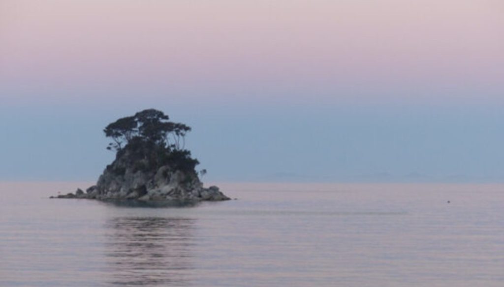 Gorgeous view of an island against a pastel pink sunset near Torrent Bay Lodge in  Abel Tasman National Park in New Zealand