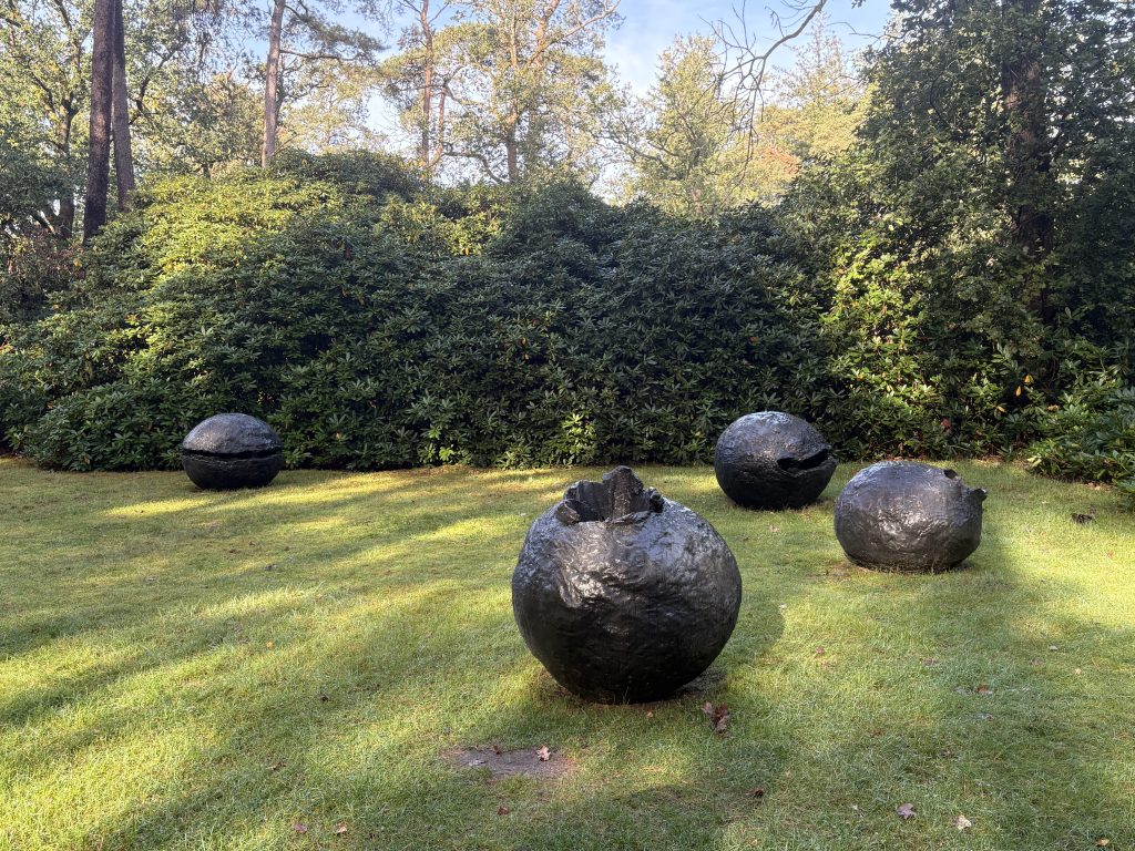Lucio Fontana's dark bronze spheres in front of a bank of rhododendrons