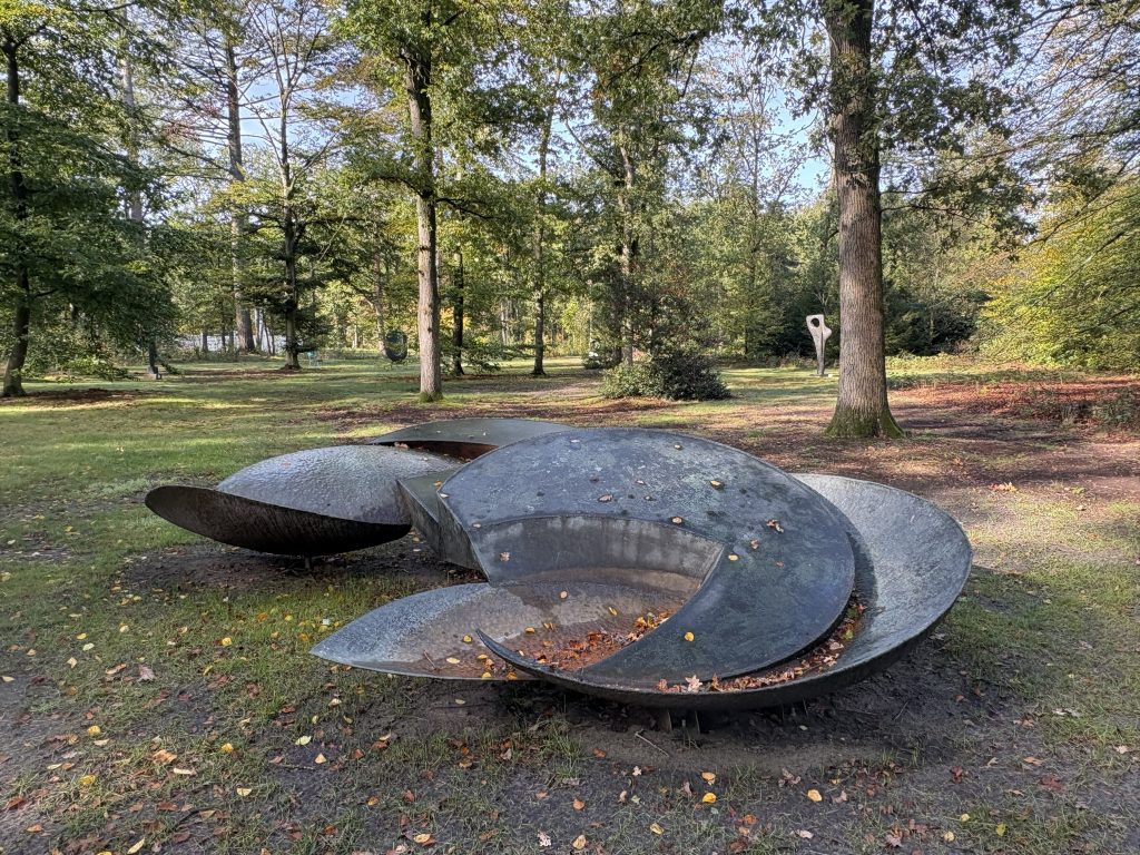 Shirazeh Houshiary's large bronze bowl forms filled with fallen leaves, with a Hepworth sculpture visible among the trees behind