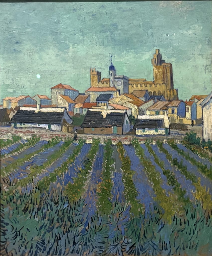 Van Gogh painting of rows of blue and green crops leading to the village and fortified church of Saintes-Maries-de-la-Mer